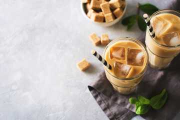 Iced coffee in tall glasses with cream and pieces of sugar, mint and straw