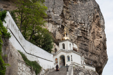 Fototapeta na wymiar Orthodox Church in the rock and monk climbing the stairs