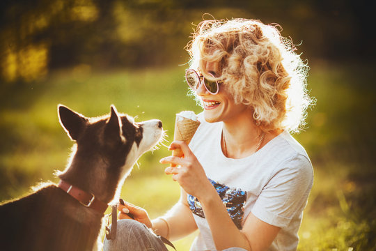 girl in glasses with ice cream in her hands is smiling at her pet in the summer in the park
