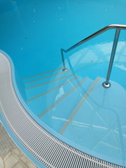 Geschwungener Beckenrand mit Gitter aus Kunststoff eines hellblau schimmernden Schwimmbeckens in...