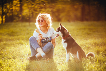 stylish girl in glasses sits cross-legged on the grass with a dog of black and white color in the park in the summer