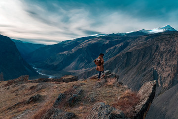 Fototapeta na wymiar Beautiful young woman with retro backpack on the top of cliff amazing mountain range landscape. Sunset. Hipster. Adventure. Travel lifestyle. Copy space.