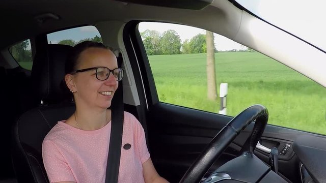 A brunette young woman with glasses drives a car - view at the driver inside 