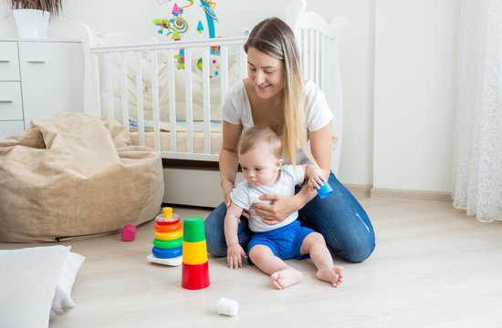Beauitufl young woman playing with her toddler son on floor at bedroom