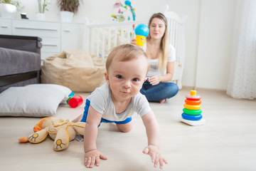 Portrait of cute 10 months old baby boy playing on floor with mother and looking at camera