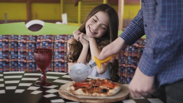 Pretty girl looking how waiter slicing a pizza for her in cafe. 4K
