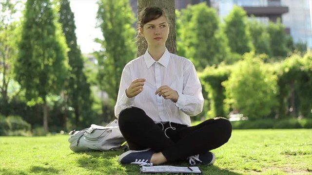 Young woman using headphones, and working in the park.