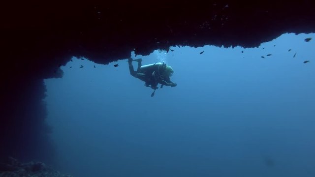 Young beautiful woman scuba diver is floating next to a cave in blue water - Indian Ocean, Maldives
