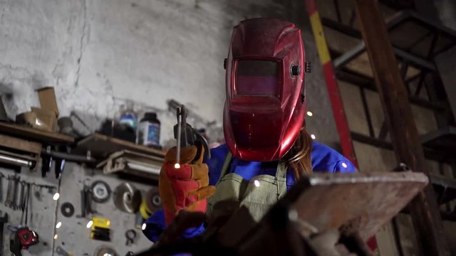 cute welder girl in uniform in the garage working with welding equipment. Women's work in art