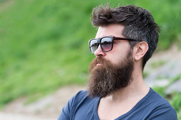 Hipster man in trendy sunglasses standing on slope with lush green glass in spring. Bearded man...