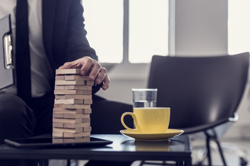 Retro toned image of businessman sitting in office building a tower of stacked blocks