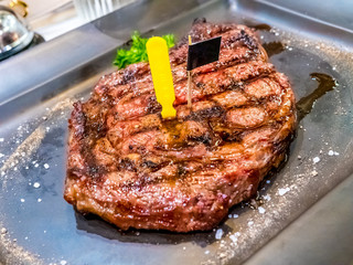 Grilled ribeye beef steak, sauce,herbs and spices on black plate. Top view with copy space for your text.