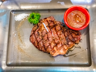 Grilled ribeye beef steak, sauce,herbs and spices on black plate. Top view with copy space for your text.