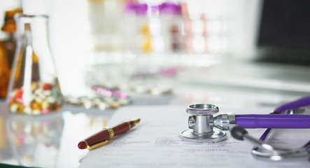 closeup of the desk of a doctors office with a stethoscope in the foreground and a bottle with pills in the background, selective focus