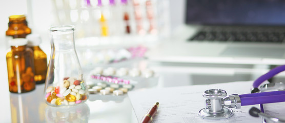 closeup of the desk of a doctors office with a stethoscope in the foreground and a bottle with pills in the background, selective focus