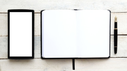 Notebook on a white wooden table next to a mobile and a pen. Top view and empty copy space for Editor's text