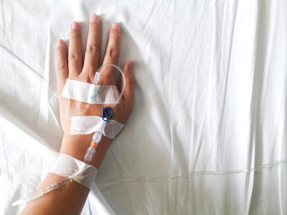 Patient hand with the tube of normal saline infusion on white cloth background