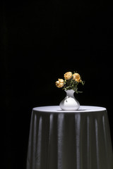 Still life with dried rose in a white vase on a black background