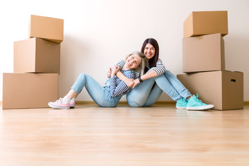 Photo of two girls sitting on floor among cardboard boxes