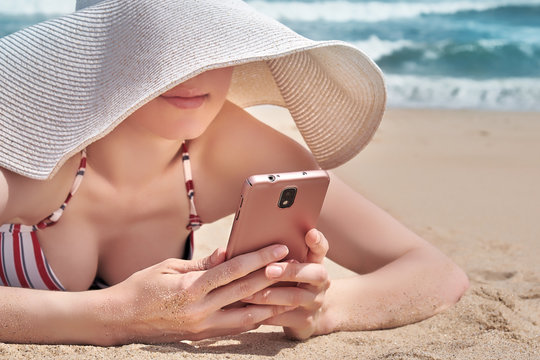 Beautiful woman using her smartphone data while relaxing on beach