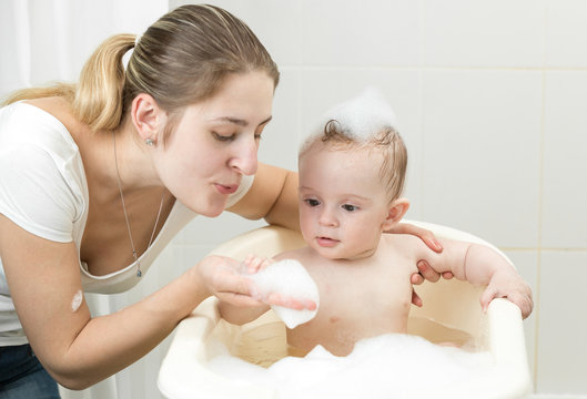 Portrait of young mother playing with her toddler boy washing in bathroom with foam