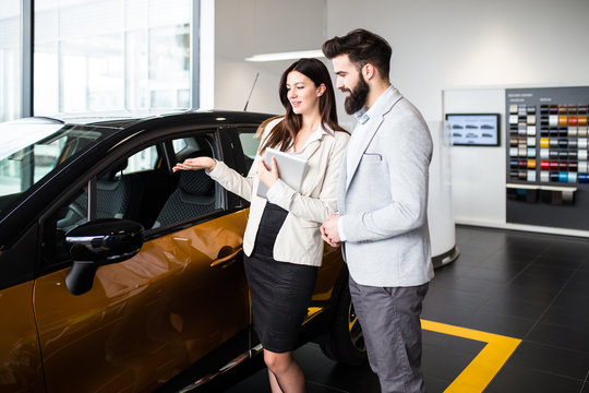 Young man talking with sales woman and choosing a new car at car showroom.
