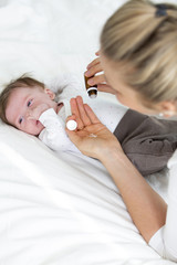 Obraz na płótnie Canvas beautiful young mother is giving her cute baby daughter homeopathic globules