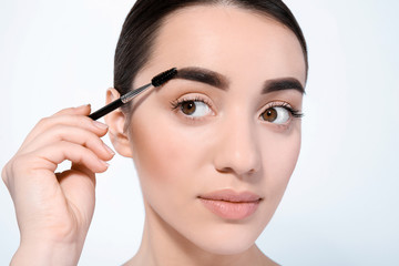 Fototapeta premium Beautiful woman with perfect eyebrows applying makeup on light background