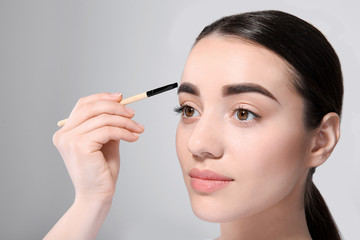 Beautiful woman with perfect eyebrows applying makeup on light background