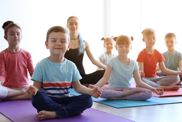 Little children and their teacher practicing yoga in gym