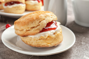 Obraz na płótnie Canvas Tasty scone with clotted cream and jam on plate, closeup