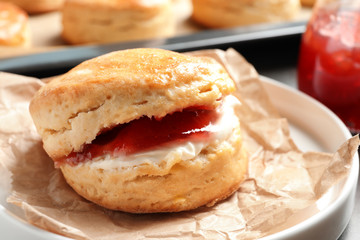 Tasty scone with clotted cream and jam on plate, closeup