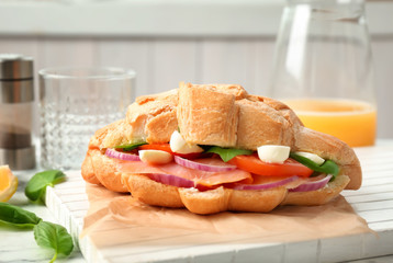 Tasty croissant sandwich with salmon on table