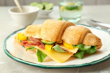 Tasty croissant sandwich with salami on table