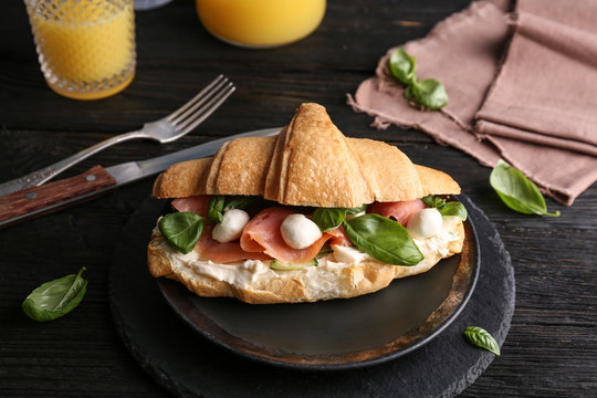 Tasty croissant sandwich with salmon on table