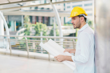 Naklejka na ściany i meble Engineer man wearing safety helmet and hold blueprint document at construction site. concept of work office, security consult, job control, development and business process.