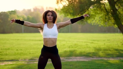 Female fitness instructor doing jumping jacks exercising in green park
