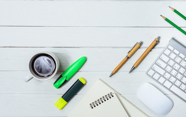 Wooden White office desk table with cup of coffee, Notebook, Pen, Marker on it.