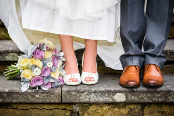Closeup of bride and groom feet and wedding bouquet of flowers