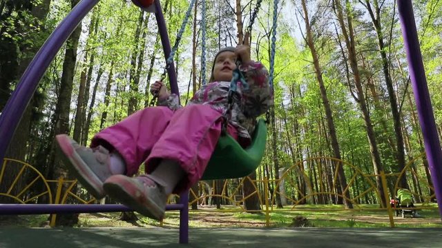 Adorable baby girl enjoying a swing ride on a playground in a park, slow motion