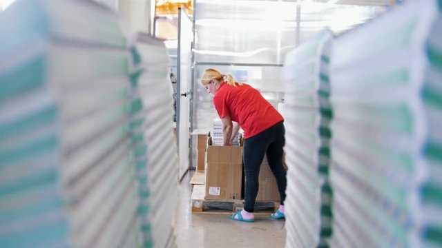 Female worker puts printed magazines in a box through the paper stacks