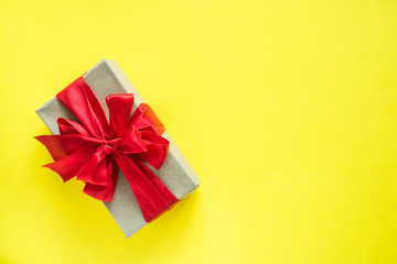Gift box with red ribbon bow on bright yellow background Copy space for text