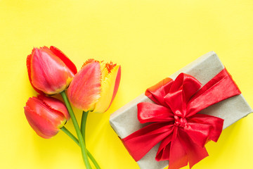 Gift box with red ribbon bow flower Bouquet tulips on bright yellow background