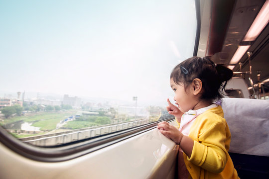 Happy And Ecxited Kids Traveling By Train. A Two Years Old Girl Pointing Her Hand To Outside View, Sitting Near Wide Glass Window And Smiling