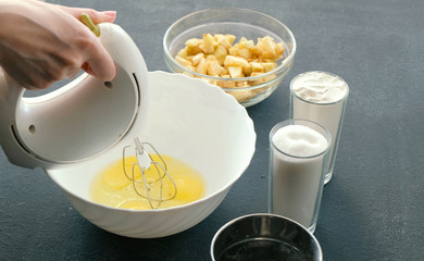 Close-up woman's hands with a mixer whisk eggs with sugar in a bowl. Cooking apple pie.