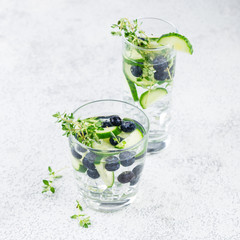 Detox infused flavored water with blueberry, cucumber and thyme on white background. Refreshing summer homemade cocktail