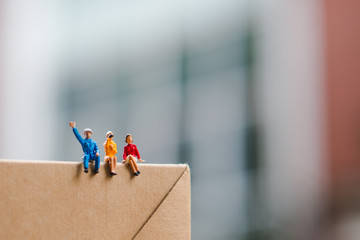 Miniature people, man and woman sitting on paper box using as business and social concept