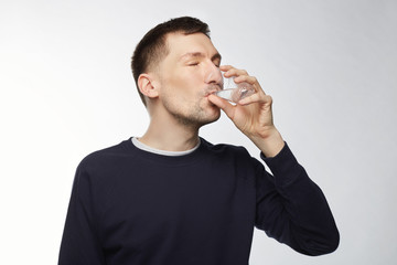 Portrait of brunet thirsty man wearing blue jacket after long training, drinks water from plastic...