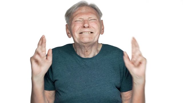 Portrait of focused pensioner man 80s having gray hair in basic t-shirt begging god please keeping fingers crossed with pathetic look, isolated over white background