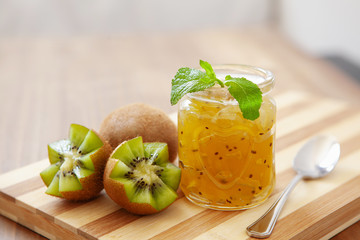 Exotic kiwi jam with ripe fruits on wooden background